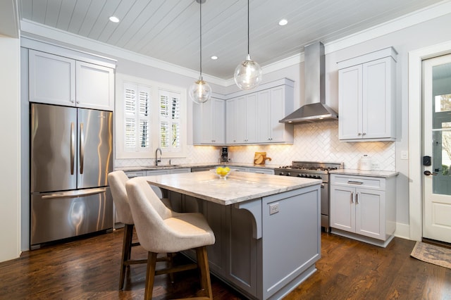 kitchen featuring a center island, appliances with stainless steel finishes, light stone countertops, wall chimney exhaust hood, and decorative light fixtures