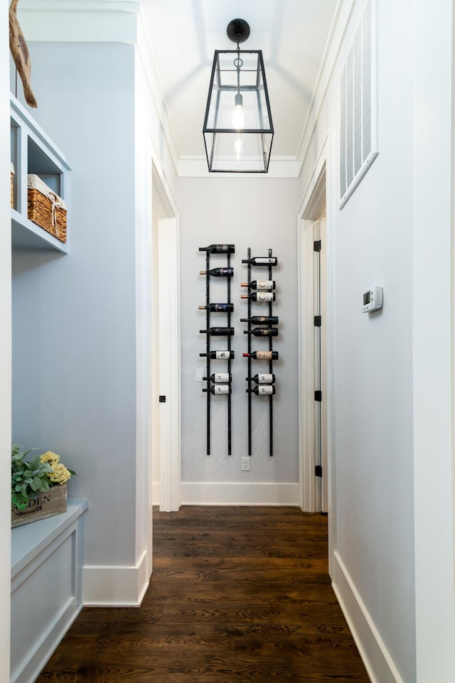 hallway with ornamental molding, dark wood-type flooring, visible vents, and baseboards