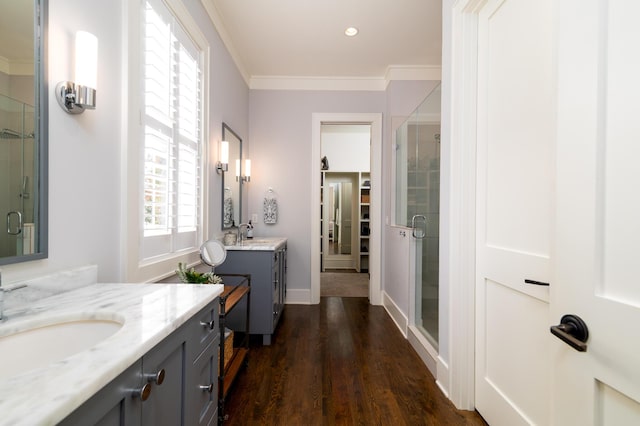 full bath with ornamental molding, wood finished floors, a sink, a shower stall, and two vanities