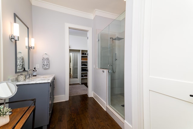 bathroom featuring a walk in closet, ornamental molding, a shower stall, vanity, and wood finished floors