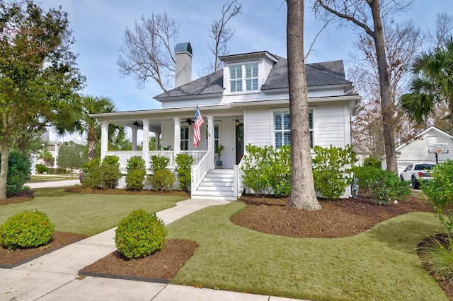 view of front of house with a shingled roof, a chimney, a porch, and a front yard