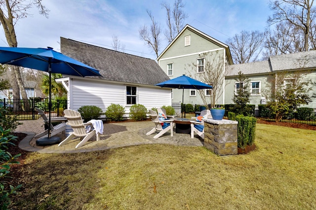 rear view of house with a patio, an outdoor fire pit, a shingled roof, fence, and a lawn