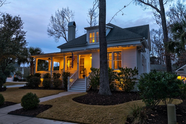 view of front of property with a chimney, a porch, a lawn, and roof with shingles