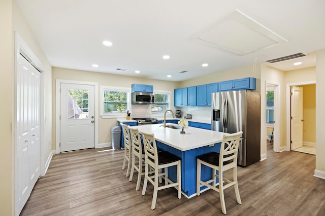 kitchen featuring appliances with stainless steel finishes, a breakfast bar area, light hardwood / wood-style flooring, and blue cabinetry