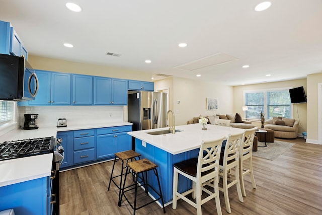 kitchen with blue cabinetry, sink, dark hardwood / wood-style floors, appliances with stainless steel finishes, and a kitchen bar