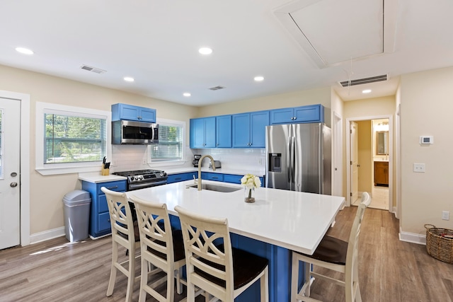 kitchen featuring appliances with stainless steel finishes, blue cabinetry, light hardwood / wood-style flooring, and a breakfast bar