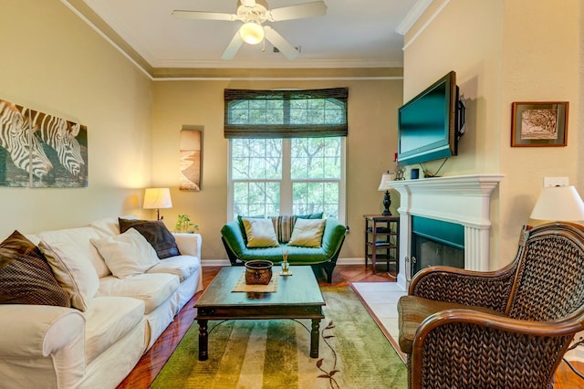 living room with wood finished floors, a fireplace with flush hearth, ceiling fan, baseboards, and ornamental molding