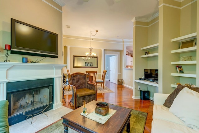 living room featuring an inviting chandelier, wood finished floors, ornamental molding, a fireplace, and built in shelves