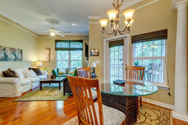 dining area featuring ornate columns, ornamental molding, light wood-type flooring, baseboards, and ceiling fan with notable chandelier
