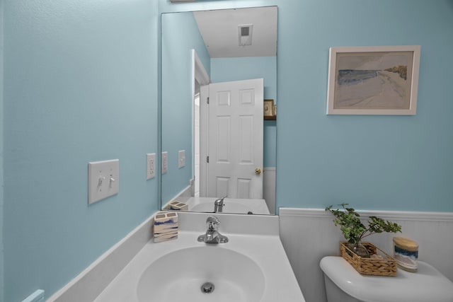 half bath featuring visible vents, wainscoting, a sink, and toilet