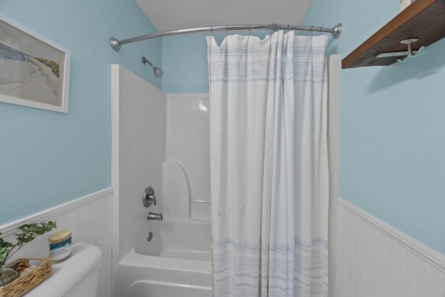 bathroom featuring a wainscoted wall, shower / bath combo with shower curtain, and toilet