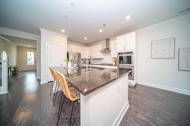 kitchen featuring white cabinetry, sink, appliances with stainless steel finishes, a center island with sink, and wall chimney range hood