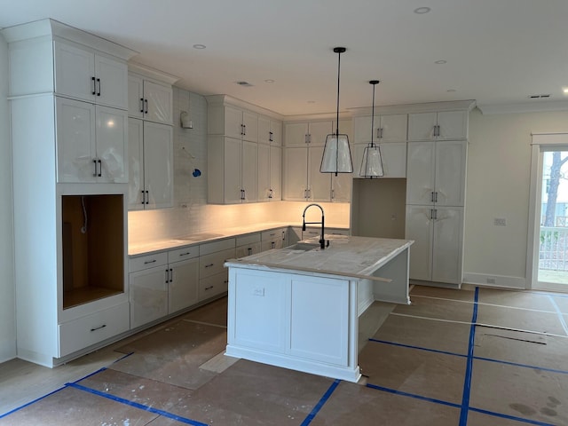 kitchen with tasteful backsplash, a kitchen island with sink, sink, and white cabinets