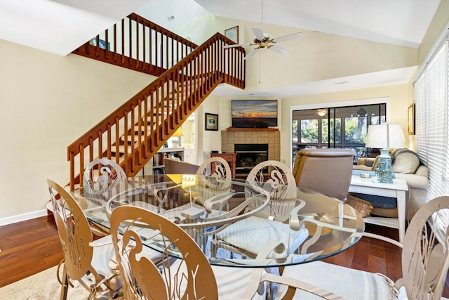 dining space with ceiling fan, wood-type flooring, a tiled fireplace, and high vaulted ceiling