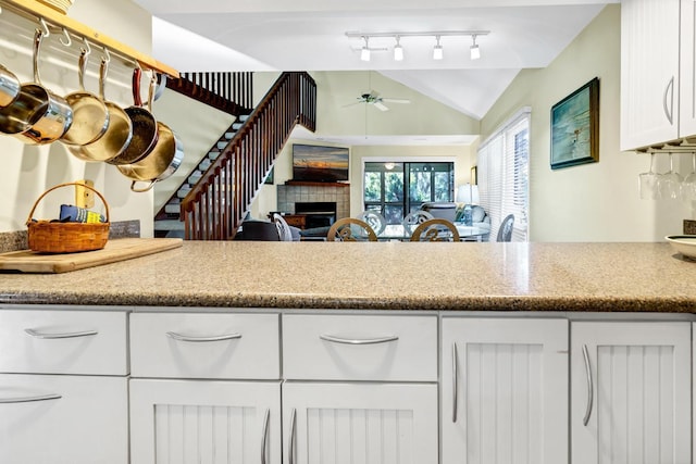 kitchen featuring lofted ceiling, light stone countertops, ceiling fan, a tiled fireplace, and white cabinets