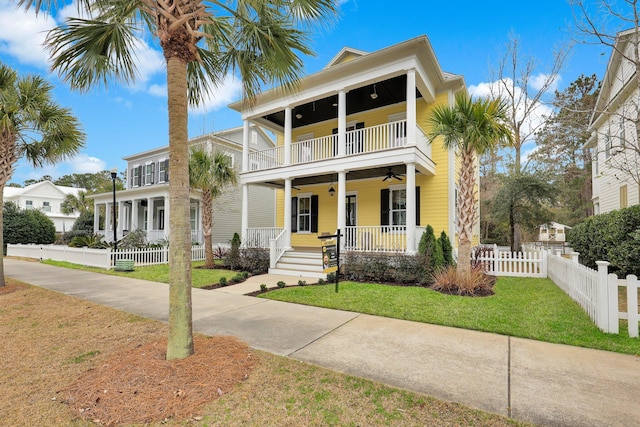 view of front of property with a ceiling fan, a balcony, covered porch, fence private yard, and a front lawn