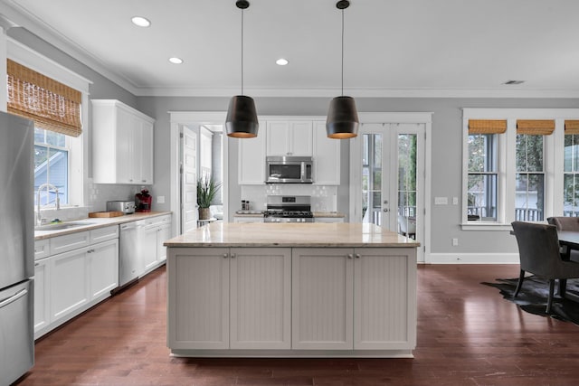 kitchen featuring a kitchen island, a sink, white cabinetry, ornamental molding, and appliances with stainless steel finishes