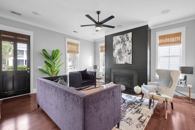 living room with visible vents, dark wood finished floors, crown molding, and a glass covered fireplace