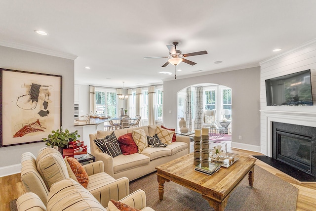 living room featuring ceiling fan, ornamental molding, a large fireplace, and light wood-type flooring