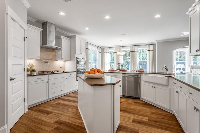 kitchen featuring appliances with stainless steel finishes, wall chimney range hood, white cabinets, and wood-type flooring