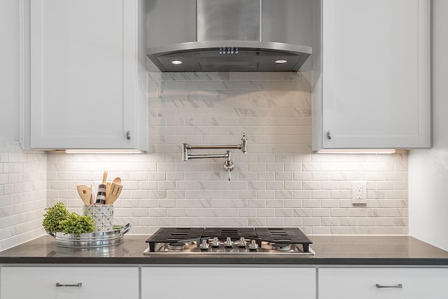 kitchen featuring wall chimney exhaust hood, stainless steel gas stovetop, tasteful backsplash, and white cabinetry