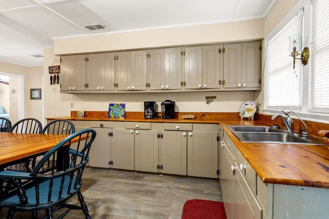 kitchen with butcher block countertops, sink, ornamental molding, and light wood-type flooring