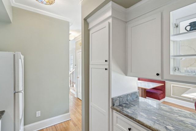 kitchen with white cabinetry, light wood-type flooring, dark stone counters, and white fridge