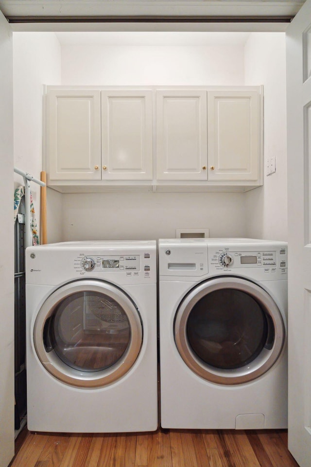 washroom with cabinets, wood-type flooring, and washer and dryer