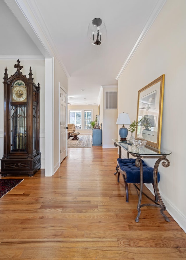 hallway featuring light wood-style floors, baseboards, ornamental molding, and visible vents