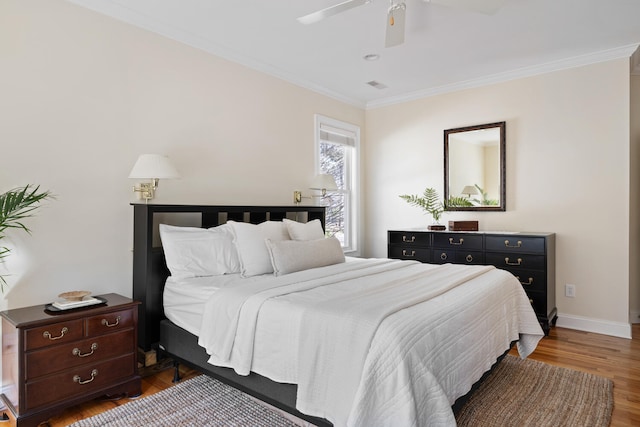 bedroom with visible vents, ornamental molding, wood finished floors, baseboards, and a ceiling fan