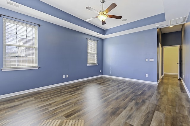 empty room with a raised ceiling, ceiling fan, plenty of natural light, and dark hardwood / wood-style flooring