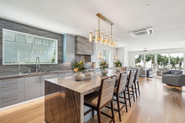 kitchen featuring ceiling fan with notable chandelier, a center island, a breakfast bar area, light wood-type flooring, and decorative light fixtures