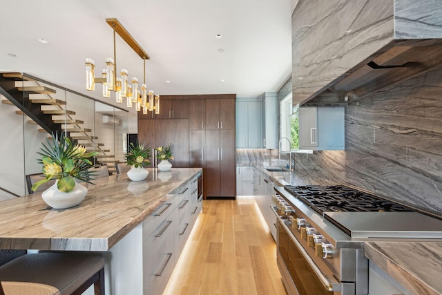 kitchen featuring light wood-type flooring, stainless steel stove, pendant lighting, decorative backsplash, and white cabinets