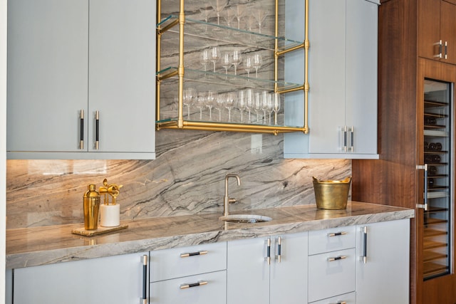 bar with white cabinetry, sink, light stone counters, and tasteful backsplash