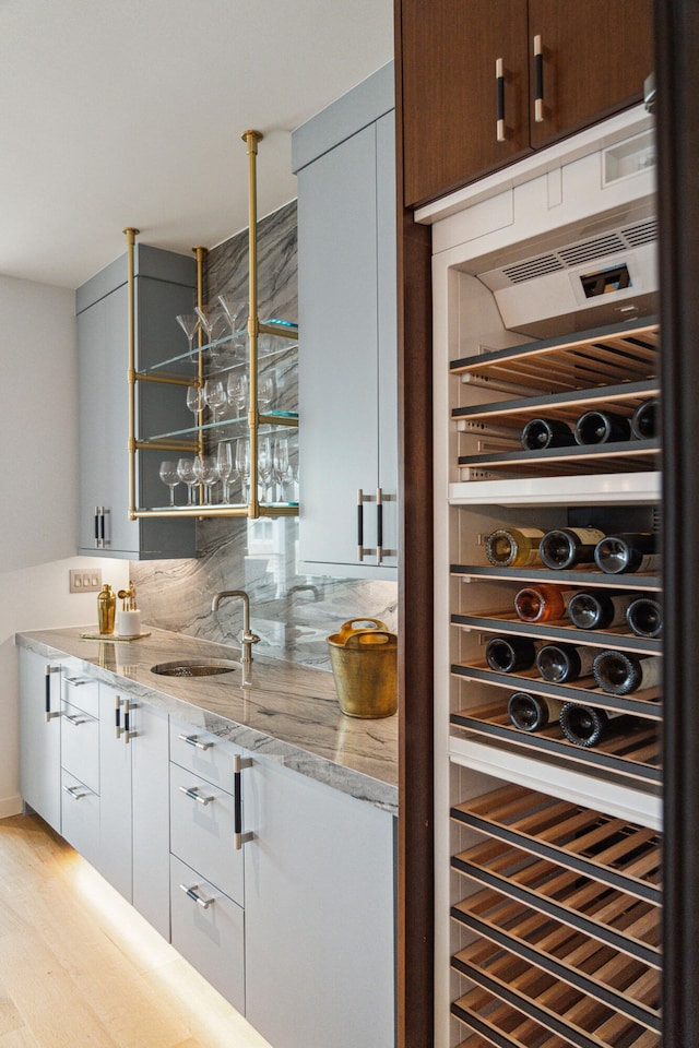 bar featuring tasteful backsplash, wine cooler, light stone countertops, sink, and light hardwood / wood-style flooring