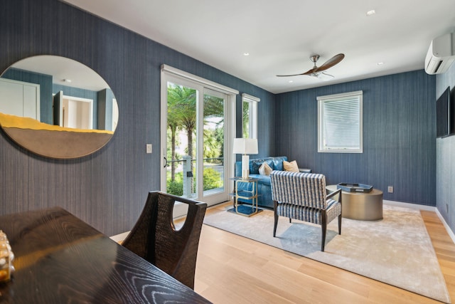 living room featuring a wall mounted air conditioner, ceiling fan, and light hardwood / wood-style flooring