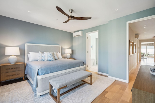 bedroom featuring a wall unit AC, light hardwood / wood-style floors, ceiling fan, and connected bathroom