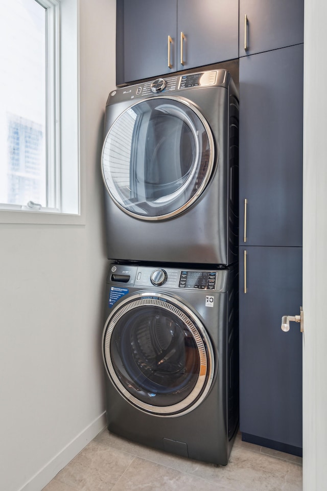 laundry area featuring cabinets, light tile patterned flooring, and stacked washer and clothes dryer