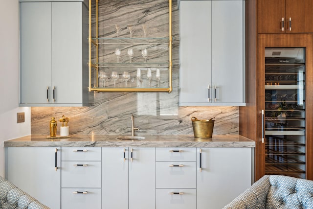 bar with white cabinetry, sink, light stone counters, tasteful backsplash, and beverage cooler