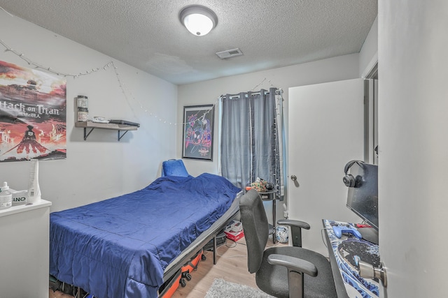 bedroom with a textured ceiling, light wood-style flooring, and visible vents