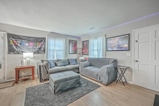 living area featuring baseboards, a textured ceiling, visible vents, and wood finished floors