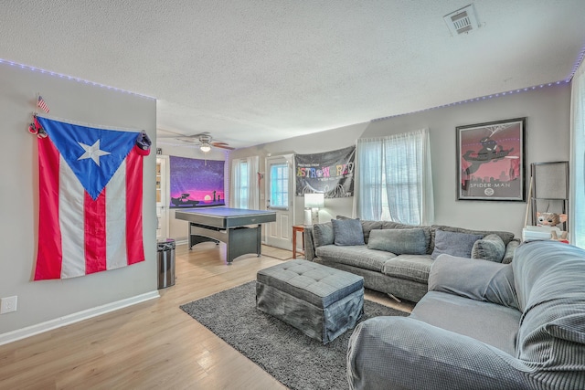 living area with a textured ceiling, light wood-type flooring, visible vents, and baseboards