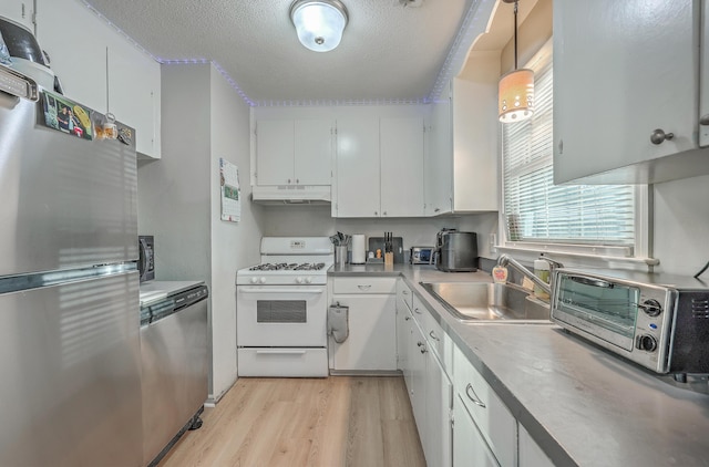 kitchen with under cabinet range hood, stainless steel appliances, a sink, white cabinets, and hanging light fixtures