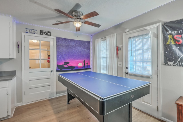 game room with light wood-style floors, ceiling fan, and a textured ceiling