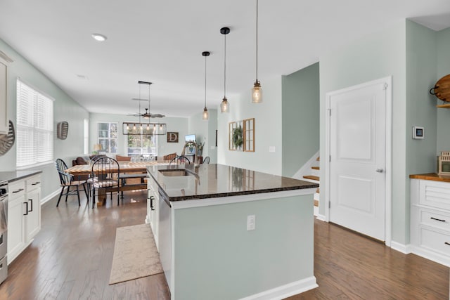 kitchen with white cabinetry, hanging light fixtures, an island with sink, and dark wood-type flooring