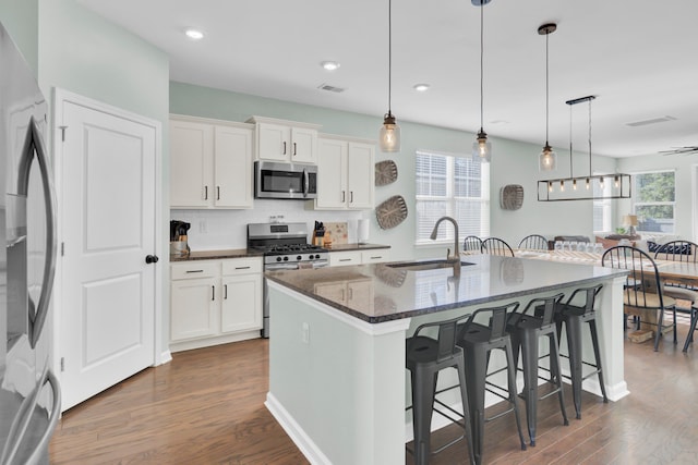 kitchen featuring stainless steel appliances, white cabinetry, a kitchen island with sink, and plenty of natural light