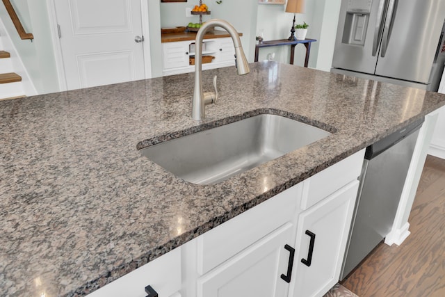 kitchen featuring dark stone counters, dark wood-type flooring, sink, dishwasher, and white cabinetry