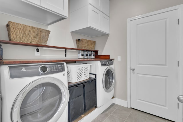 clothes washing area with washer and dryer, light tile patterned flooring, and cabinets