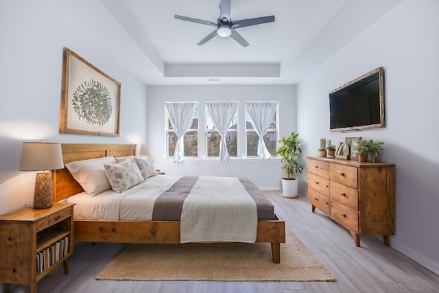 bedroom with ceiling fan, light wood-type flooring, and a tray ceiling