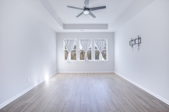 spare room featuring a tray ceiling, ceiling fan, and light wood-type flooring